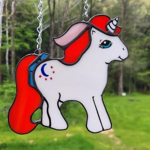 May include: A stained glass unicorn with a red mane and tail, a white body, and a blue and silver crescent moon and stars on its flank.