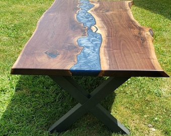 May include: A live edge walnut wood table with a blue epoxy river running through the center. The table has a black X-shaped base.