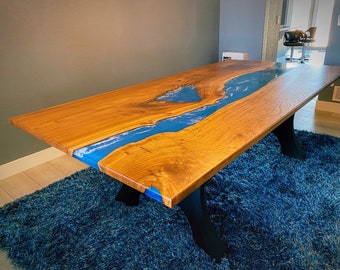 Pode incluir: Uma mesa de jantar de madeira com um rio de epóxi azul que atravessa o centro. A mesa tem pernas de metal preto e está sobre um tapete azul.