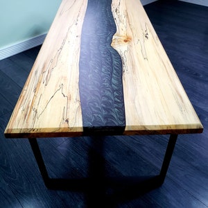 May include: A wooden coffee table with a black resin river running down the centre. The table has a natural wood finish and black metal legs.