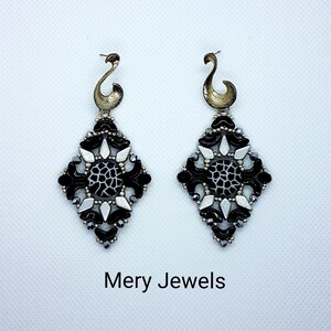 May include: A pair of black and white dangle earrings with a geometric design. The earrings feature a black and white patterned center piece and are accented with silver and black beads. The earrings are labeled "Mery Jewels".