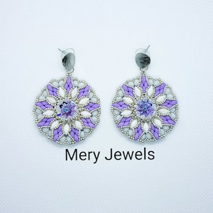 May include: A pair of dangle earrings with a purple and white beaded design. The earrings feature a large, round, beaded centerpiece with a clear crystal in the center. The earrings are silver-toned and have a simple hook closure.