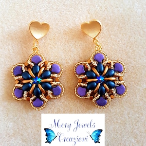 May include: Purple and gold star-shaped earrings with a blue crystal in the centre. The earrings are hanging from gold heart-shaped posts. The earrings are labelled "Mery Jewels Creazioni".
