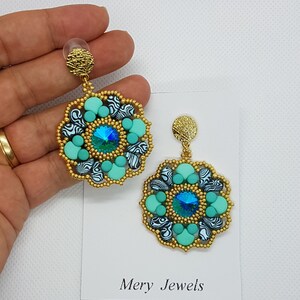 May include: A pair of gold dangle earrings with a turquoise and black patterned design. Each earring features a large turquoise gemstone in the center.