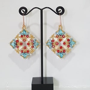 Peut inclure: Une paire de boucles d'oreilles carrées en perles dorées, rouges et bleues. Les boucles d'oreilles sont suspendues à un support à boucles d'oreilles noir.