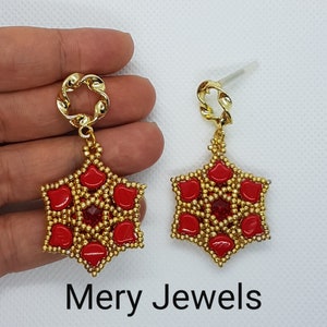 Op de afbeelding: Een paar gouden oorbellen met rode en gouden kralen in de vorm van een ster. De oorbellen hangen aan een gouden ketting.