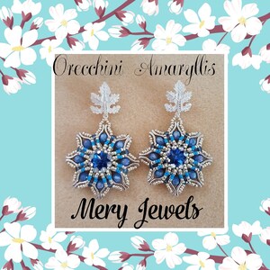 Può includere: Un paio di orecchini a forma di fiocco di neve blu e argento con un ciondolo a foglia d'argento. Gli orecchini sono etichettati "Orecchini Amaryllis" e "Mery Jewets".