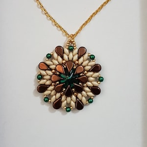 Può includere: Una collana con catena dorata con un ciondolo fatto di perline marroni, bianche e verdi. Il ciondolo è di forma circolare con una pietra preziosa verde al centro.
