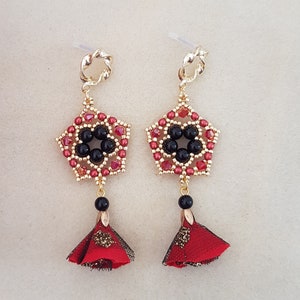 May include: A pair of gold earrings with red and black beaded star-shaped charms and red tassel pendants.