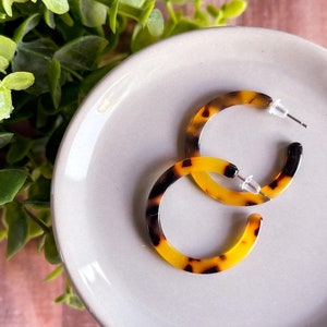 May include: A pair of brown and yellow hoop earrings with a tortoiseshell pattern. The earrings are on a white plate.
