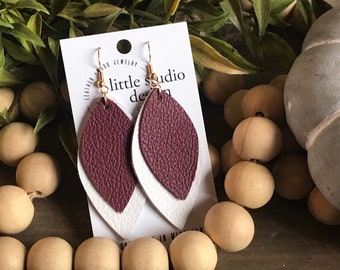 May include: A pair of dangle earrings with a burgundy and white leather design. The earrings are on a white card with the text "little studio design".