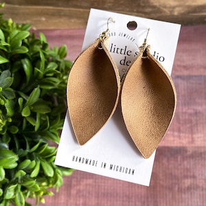 May include: A pair of brown leather earrings with gold hooks. The earrings are shaped like teardrops and have a textured surface. The earrings are handmade in Michigan.
