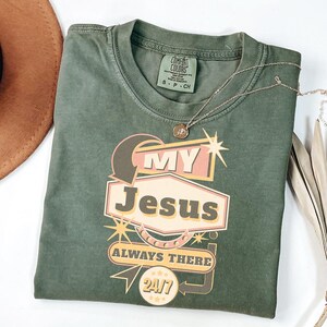 May include: A green t-shirt with a retro-style graphic that says "My Jesus Always There 24/7".