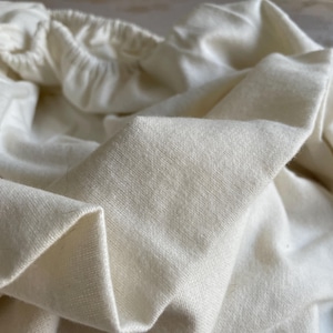 Könnte beinhalten: Nahaufnahme eines weißen Baumwollstoffs mit glatter Textur. Der Stoff ist gefaltet und zeigt das weiche, natürliche Material.