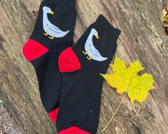 May include: A pair of black socks with red trim and a white duck design. The socks are on a wooden surface with a yellow leaf.