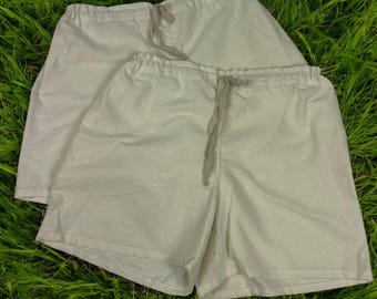 May include: Two pairs of off-white cotton shorts with drawstring waists. The shorts are folded and laid out on a bed of green grass.