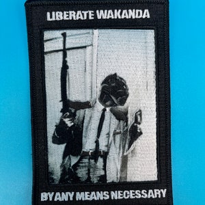 May include: Black and white embroidered patch with the text "Liberate Wakanda" and "By Any Means Necessary". The patch features a black and white image of a person holding a rifle.