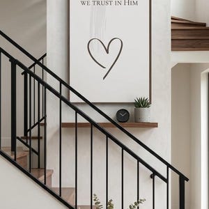 May include: A vertical sign with the text "In this home" and inspirational phrases. A black clock and potted plant sit on a shelf. A blue bench with a green throw and a vase of greenery are below.