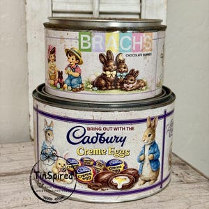 May include: Two vintage metal tins, one stacked on the other, featuring Easter-themed graphics. The top tin displays "Brach's Chocolate Bunnies" with children and bunnies. The bottom tin showcases "Cadbury Creme Eggs" with bunny illustrations.