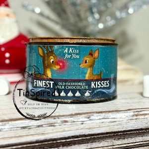May include: A distressed tin with a blue background, depicting reindeer and the text "A Kiss for You." The tin is labelled "Finest Old-Fashioned Milk Chocolate Kisses." The product is sold on Etsy.