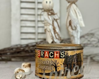 May include: A vintage-style tin of "Brach's Toasty Ghosties" with a Halloween theme. The tin is accompanied by two handmade ghost figures and two toasted marshmallows. The label features a haunted house illustration.