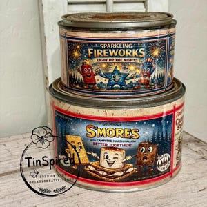 Peut inclure: Deux boîtes métalliques vintage, l'une empilée sur l'autre. La boîte supérieure indique "Sparkling Fireworks, Light Up The Night!" avec des personnages de feux d'artifice de dessins animés. La boîte inférieure dit "Delicious S'mores with Campfire Marshmallow Better Together!" avec des personnages de s'mores de dessins animés.