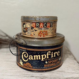 Peut inclure: Deux boîtes métalliques vintage sur le thème d'Halloween. La boîte supérieure porte l'inscription "Brach's Candy Corn" avec des illustrations de momie, de chat et de bonbons. La boîte inférieure porte l'inscription "Campfire Spooky Marshmallows".