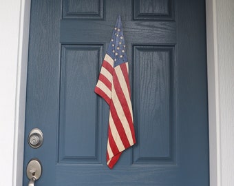 Op de afbeelding: Een blauwe voordeur met een kleine Amerikaanse vlag die eraan hangt.