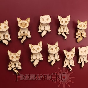 May include: A collection of ten wooden cat cutouts, each with unique markings and poses. The cats are light brown with detailed facial features and sit on a deep red background. The text "TIMBERLAND CNC" is at the bottom.