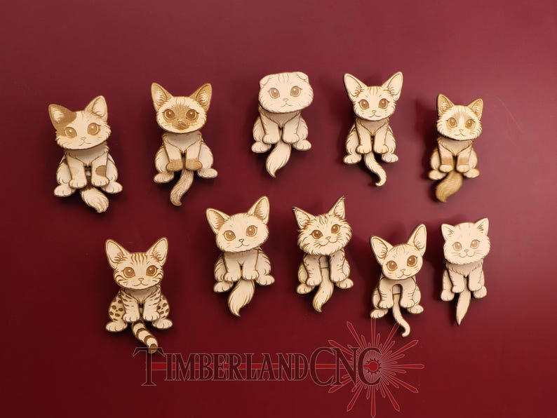 May include: A collection of ten wooden cat cutouts, each with unique markings and poses. The cats are light brown with detailed facial features and sit on a deep red background. The text "TIMBERLAND CNC" is at the bottom.