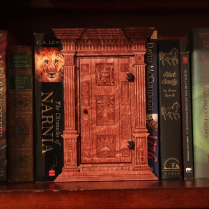 K&ouml;nnte beinhalten: Ein B&uuml;cherregal mit einer Auswahl an B&uuml;chern, darunter Harry Potter, Die Chroniken von Narnia und Black Beauty. Das B&uuml;cherregal ist aus dunklem Holz gefertigt und hat eine dekorative Holzt&uuml;r in der Mitte.