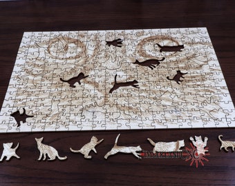 May include: A wooden jigsaw puzzle featuring a cat's face and several cat silhouettes. The puzzle pieces are light brown, with a detailed image of a cat's face. Several cat-shaped pieces are separate from the puzzle, and the logo "TIMBERLAND CNC" is visible.