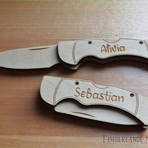 May include: Two wooden pocket knives, one open and one closed, with the names "Alivia" and "Sebastian" engraved on the handles. The knives are light brown and rest on a wooden surface. The blades are silver.