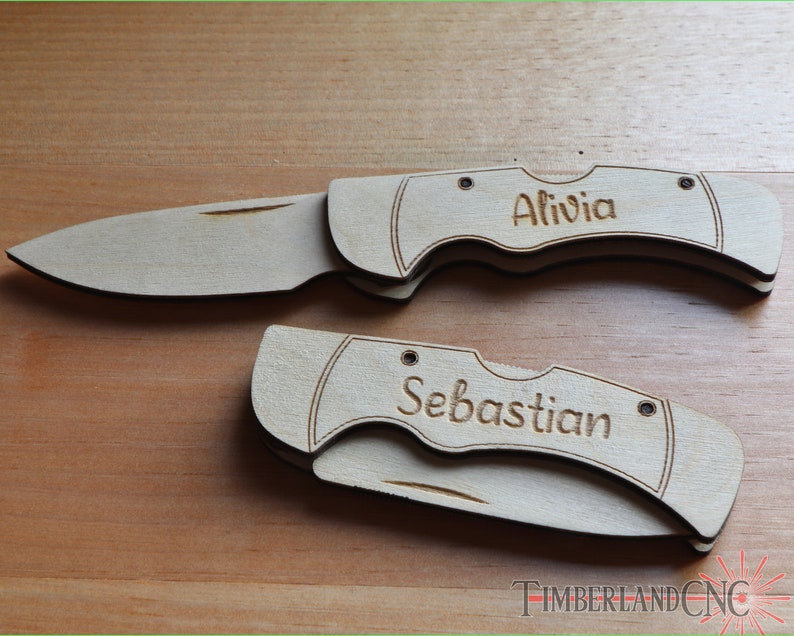 May include: Two wooden pocket knives, one open and one closed, with the names "Alivia" and "Sebastian" engraved on the handles. The knives are light brown and rest on a wooden surface. The blades are silver.
