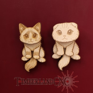 May include: Two light-colored wooden cat cutouts with engraved details. The left cat has pointed ears and a fluffy tail, while the right cat has folded ears and a smooth tail. The text TIMBERLANDCNC is visible at the bottom in red.