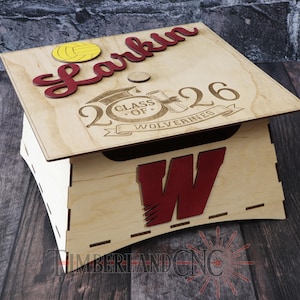 May include: Wooden graduation box with a lid. The lid features the name "Larkin" in red, a yellow volleyball, and the text "Class of Wolverines 2026". The box has a red "W" on the front.