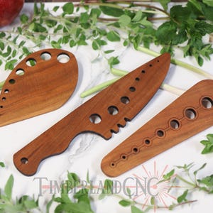 Peut inclure: Trois ustensiles de cuisine en bois avec des découpes. Les ustensiles sont en bois brun clair et ont des formes et des tailles variées. Les ustensiles sont disposés sur une surface blanche avec des plantes vertes feuillues.