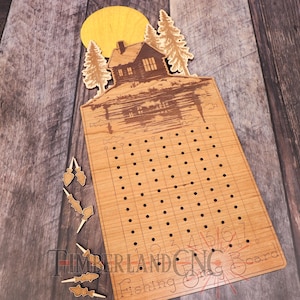 May include: Wooden fishing game board with a cabin and lake scene, a yellow sun, and several wooden fish-shaped pegs. The board has a grid of holes for peg placement and the numbers 1-7. The words "Fishing Board" are visible.