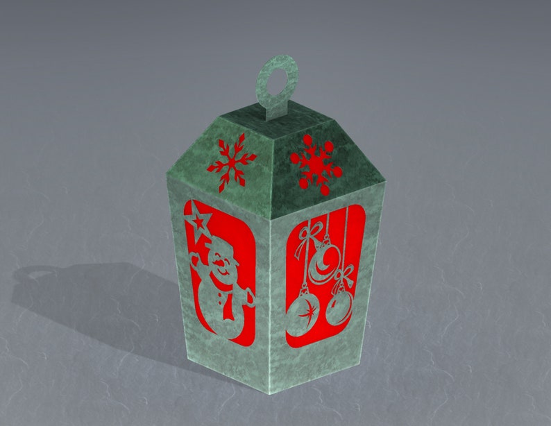 May include: A green paper lantern with a red snowman and snowflake designs. The lantern has a loop at the top for hanging.