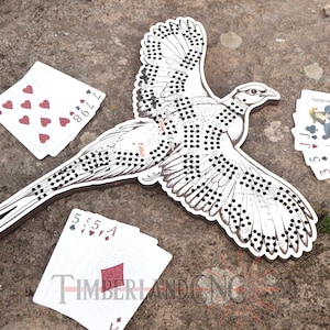 May include: A wooden cutout of a bird in flight, with intricate dot and line details. Playing cards with red and black suits are scattered around the bird. The bird's wings are spread, and the design is in black and white.
