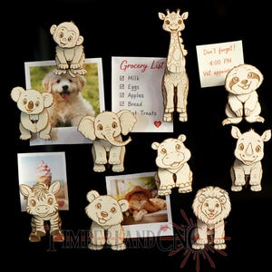 Peut inclure: Ensemble d'aimants en bois représentant des animaux, dont une girafe, un singe, un koala, un éléphant, un zèbre, un ours, un lion, un hippopotame, un rhinocéros et un paresseux. Ils sont fixés sur une surface noire.