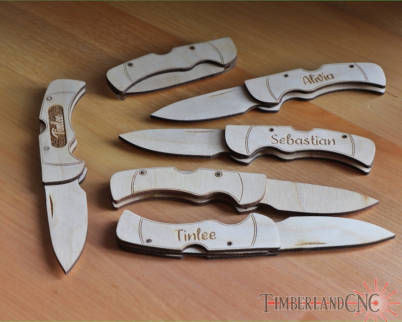 May include: A collection of wooden pocket knives, some engraved with names like "Alivia", "Sebastian", and "Tinlee". The knives are light brown and feature a classic folding design. The image is taken on a wooden surface.