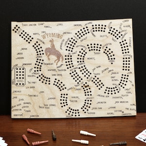 May include: A wooden game board with a map of Wyoming and the names of cities and towns throughout the state. The board is designed for a game of peg solitaire.