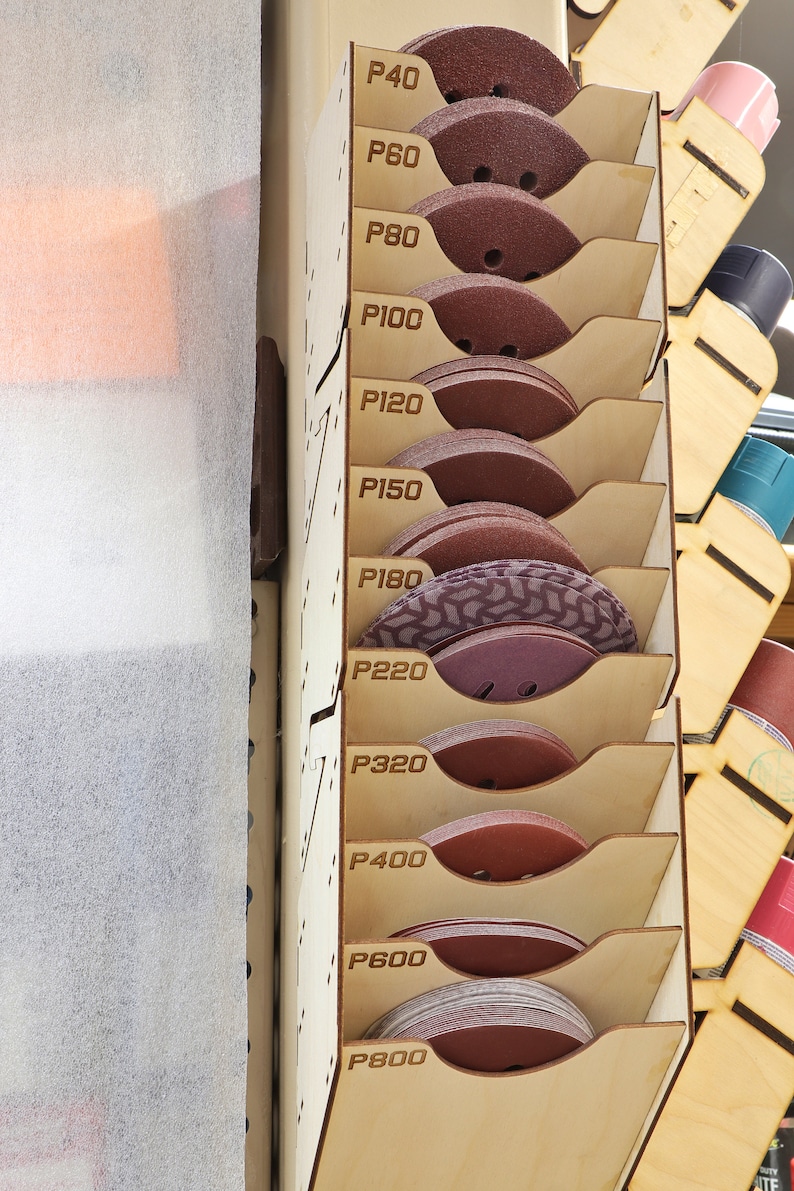 Puede incluir: Un estante de madera con 10 estantes que contienen varios discos de papel de lija. El papel de lija est&aacute; etiquetado con n&uacute;meros de grano de P40 a P800.