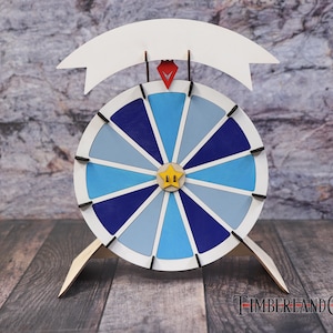 May include: A wooden prize wheel with a white banner, a red gem, and a yellow star. The wheel features segments of blue, light blue, and white. The wheel is supported by two wooden legs. The background is a textured grey and brown.