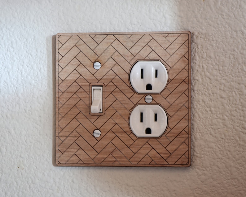 May include: A wooden wall plate with a herringbone pattern, featuring a light switch and a double electrical outlet.