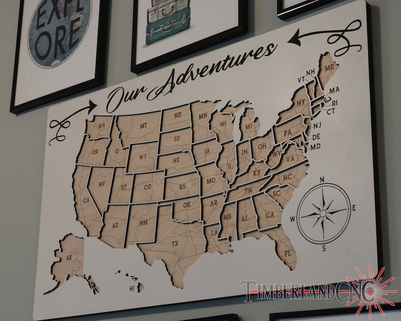 May include: A wooden map of the United States with the text "Our Adventures" at the top. Each state is outlined and labeled with its abbreviation. The map includes Alaska and Hawaii. A compass is in the lower right corner.