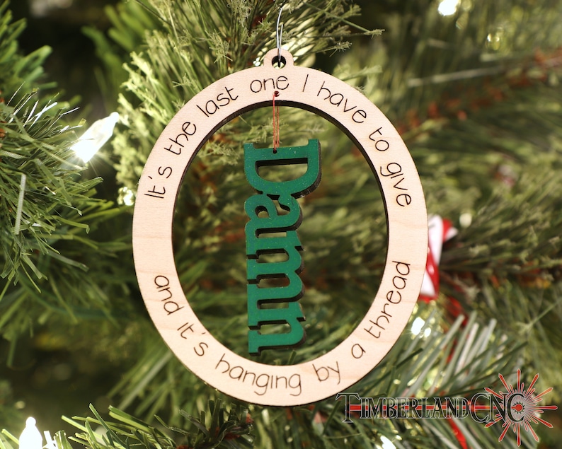 May include: A wooden Christmas ornament with the text "It's the last one I have to give and it's hanging by a thread" and the word "Damn" in green inside the circle.