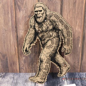 May include: A brown wooden cutout of Bigfoot, a mythical creature, walking with a detailed design of fur and a beard. The cutout is against a woodgrain background.