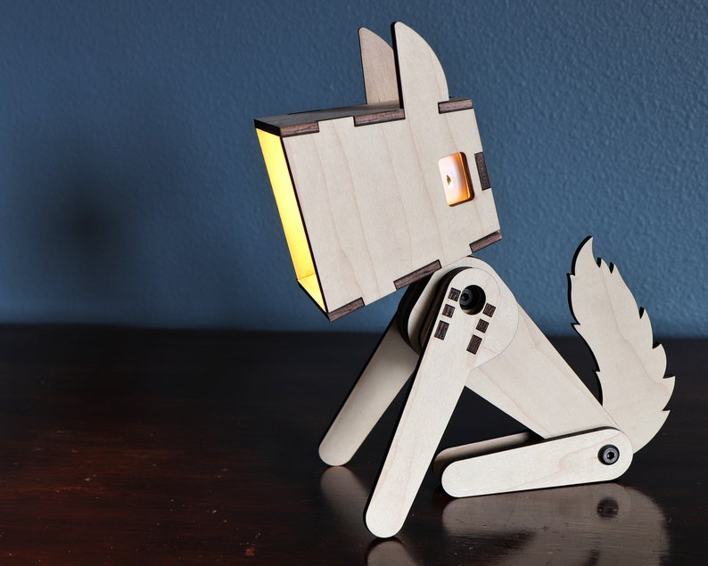 以下が含まれることがあります： 頭から光が漏れている木製の犬のランプ。犬は木製のテーブルの上に座っています。